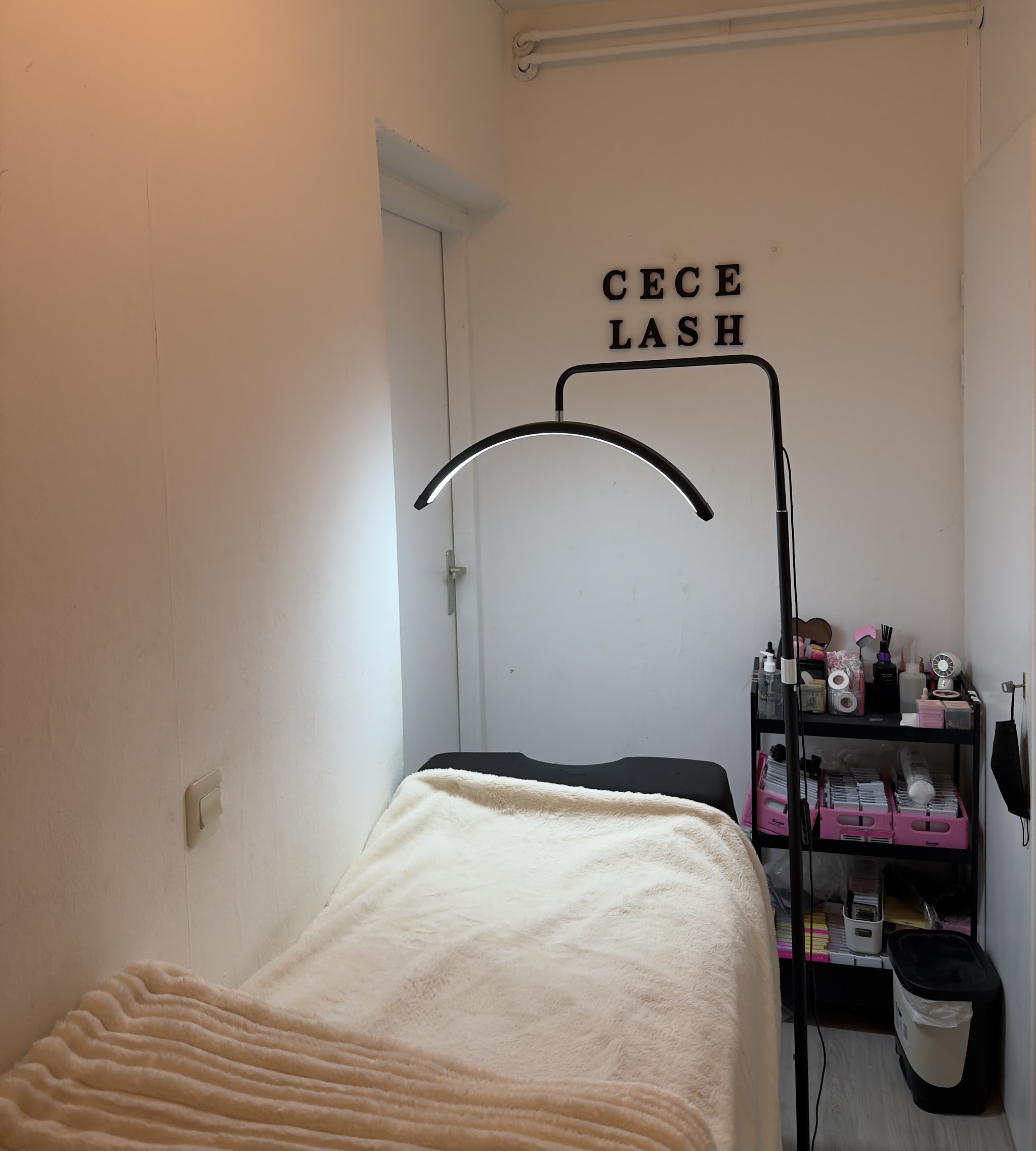 De studio van Cece Lashh: het behandelbed met crèmekleurige deken, de lamp en de letters CECE LASH op de muur
