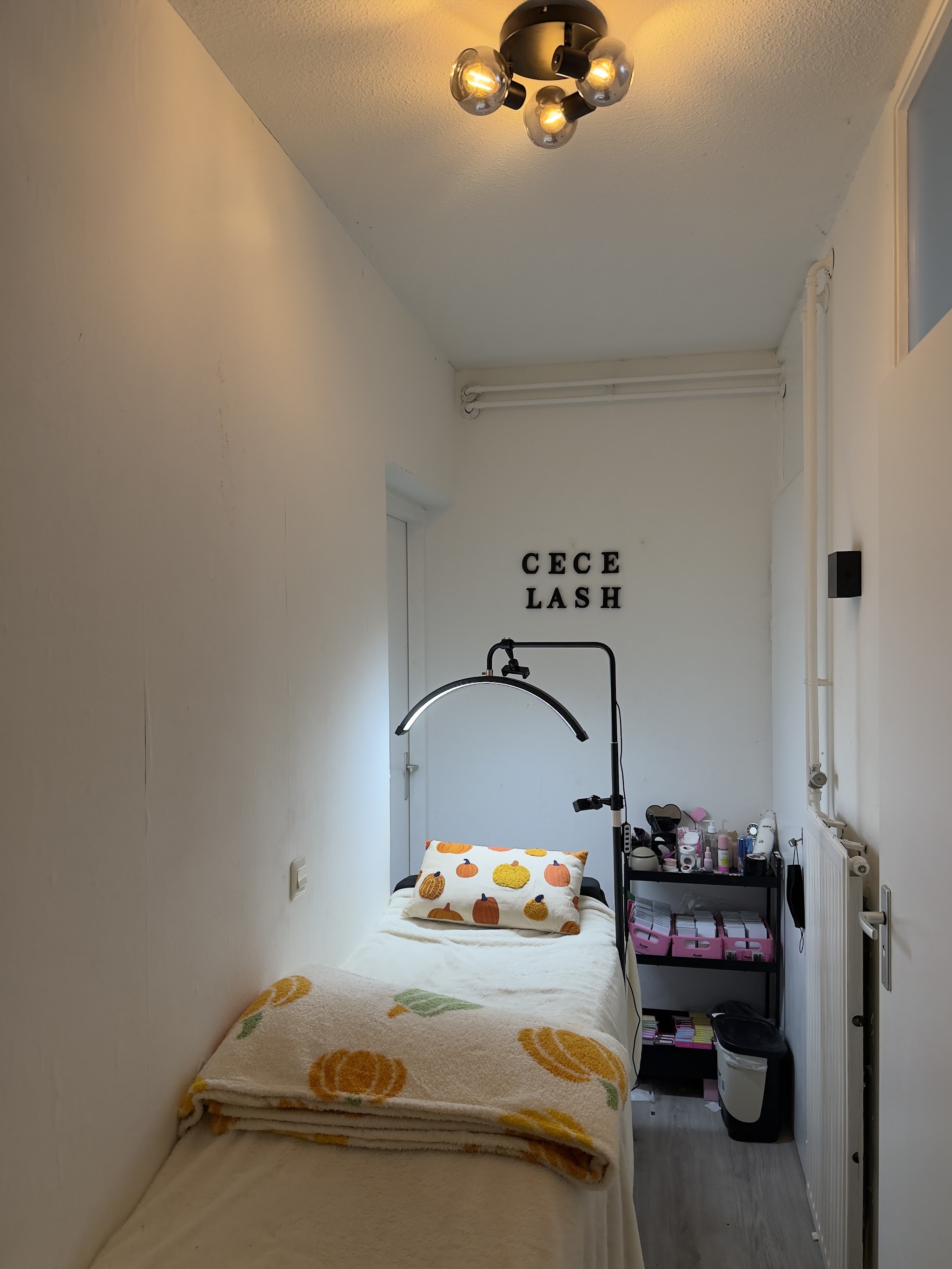 Doorkijk naar het behandelbed in de studio van Cece Lashh, met de lamp en de letters CECE LASH